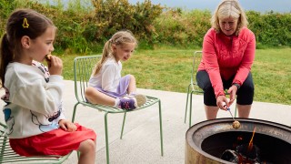 A mother and two young girls toast marshmallows over a fire on bere island.