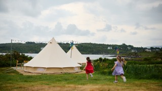 Children run across grass towards a bell tent on Bere Island