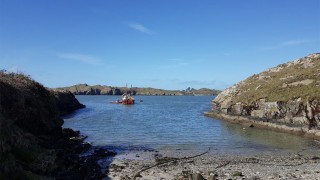 Faraway shot of the Sherkin Island Ferry surrounded by a rocky coastline