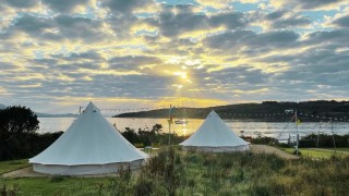 Two bell tents on a grassy hill on Bere Island overlooking the sea and the sunset